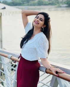 a woman standing on a bridge next to the water with her arms behind her head