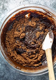 a glass bowl filled with brownie batter and a wooden spoon in the bowl next to it