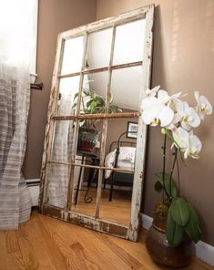 a mirror sitting on top of a hard wood floor next to a vase with flowers