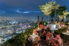 people sitting at tables on top of a high rise with city lights in the background