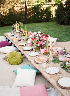 a long table with plates and flowers on it in the middle of a yard area