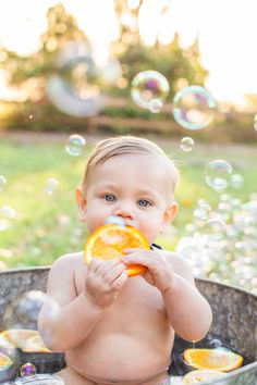 a baby sitting in a tub holding an orange