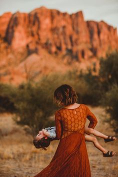 a woman holding a child in her arms while standing next to a large rock formation