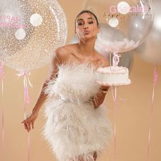 a woman in a white dress holding a cake and some balloons with pink streamers