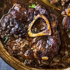 a pot filled with meat and mushrooms covered in gravy next to a spoon