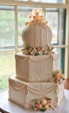 a three tiered white wedding cake with flowers on the top and sides, sitting in front of a window