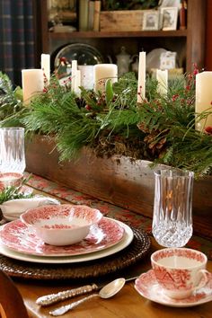 a dining room table set for christmas with candles and dishes on the placemats