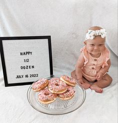 a baby sitting next to a plate of doughnuts