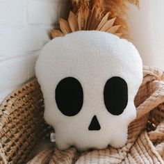 a white skull stuffed animal sitting on top of a bed next to a plant in a wicker basket