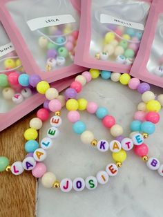 three personalized beaded bracelets with name charms on them sitting on a table