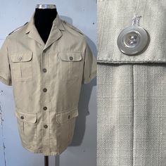 Lovely beige over shirt - jacket - safari style - open neck . 5 buttons - 4 pockets - short sleeve - epaulettes .2 vents on either side at hem ... see pics ..  Fabric has a check slub running through size label says 40"/42"... medium / large depending on desired fit .. see measurements  pit to pit 23"(46") length 31" shoulder to shoulder 18.5"  condition is great Beige Summer Camp Shirt With Pockets, Summer Single Breasted Short Sleeve Top, Summer Short Sleeve Single Breasted Top, Summer Single-breasted Short Sleeve Top, Collared Camp Shirt With Pockets For Work, Beige Camp Collar Shirt With Button Closure, Beige Camp Collar Shirt With Buttons, Short Sleeve Camp Shirt With Pockets For Work, Collared Summer Outerwear With Button Closure