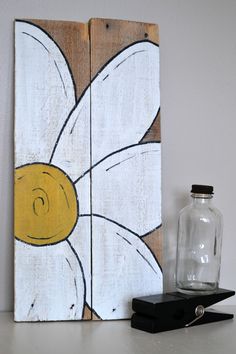 a wooden sign with a flower painted on it next to a glass bottle and pen