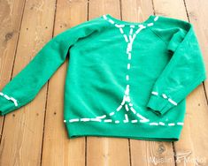 a green sweater with white stitching on it sitting on a wooden floor next to a pair of scissors