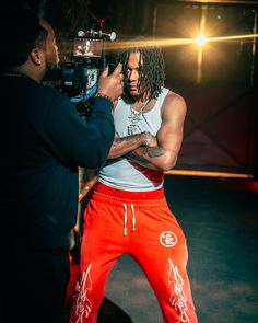 a man with dreadlocks is being filmed by another man in red sweatpants