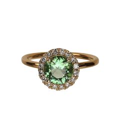 a ring with an oval cut green stone surrounded by small white and yellow diamond halos