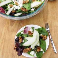 a salad with apples and walnuts in it on a white plate next to a fork