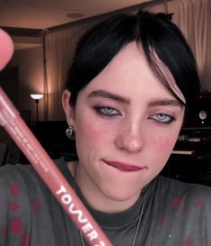 a woman is holding a pink pencil in her right hand and looking at the camera