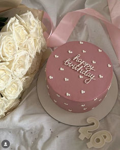 a pink birthday cake next to a bouquet of white roses