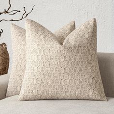 two pillows sitting on top of a couch next to a vase