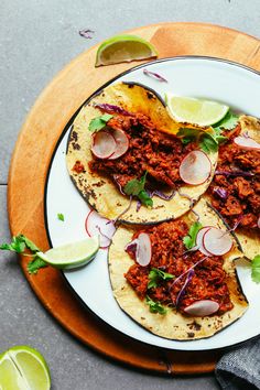 three tacos on a plate with limes and cilantro next to them