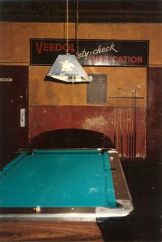 a pool table with a light hanging from it's ceiling in front of a sign that reads veedcil