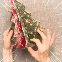 two hands are holding an origami christmas tree on top of a tablecloth