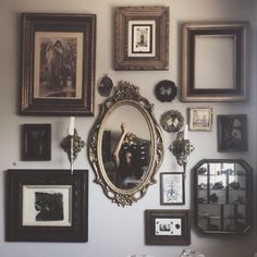 there are many framed pictures on the wall and one is holding up a hand mirror