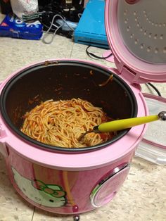 a pink crock pot filled with noodles on top of a counter next to an open lid