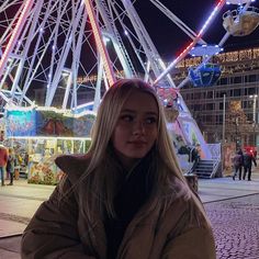 a woman standing in front of a ferris wheel at night