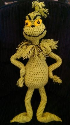 a crocheted figure is posed on a black surface with yellow eyes and hair