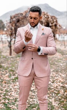 a man in a pink suit and white shirt is looking down at his hand while standing in the grass