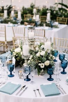 the table is set with blue and white place settings, silverware, candles, and flower centerpieces