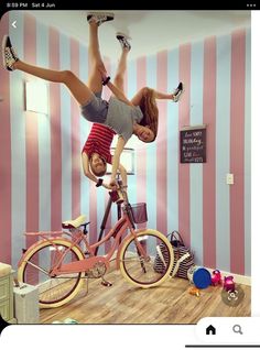 a woman is doing tricks on a bicycle in a room with pink and white striped walls