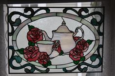 a stained glass window with red roses and a teapot on the table next to it