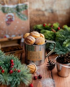 some cookies are in a metal mug on a table next to pine cones and evergreens