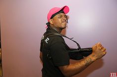 a man wearing a pink hat and black shirt with tattoos on his chest is standing in front of a purple wall