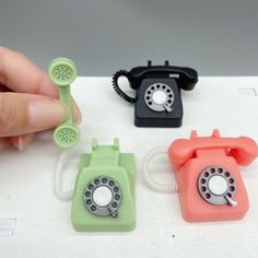 three telephones sitting on top of a white table with one being held up by a hand