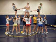 a group of young women standing on top of each other in front of a basketball court