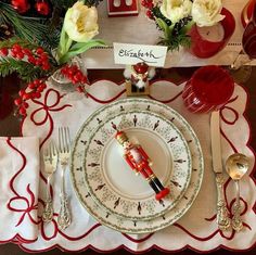 a christmas table setting with red and white place mats, silverware, napkins, and candlesticks