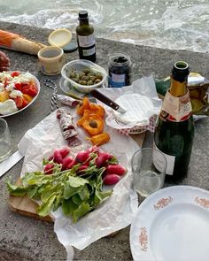 an assortment of food is laid out on a table next to the ocean and wine bottles