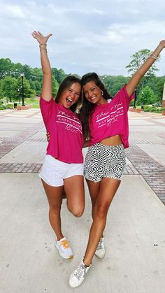 two women in pink shirts and white shorts posing for the camera with their arms up