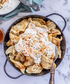 a skillet filled with pasta and sauce on top of a white counter next to two bowls