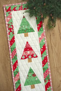 a quilted christmas tree table runner on a wooden floor next to a potted plant