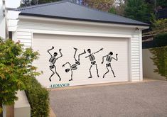 a garage door decorated with skeletons dancing in front of a white building and green trees