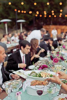 several people sitting at a long table with plates of food