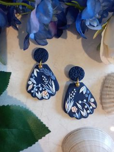 two pairs of blue and white earrings sitting on top of a table next to flowers