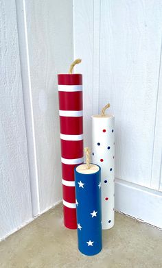 three different colored candles sitting next to each other on the floor in front of a white wall