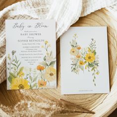 two yellow and white flowers are on top of the wedding stationery, next to each other