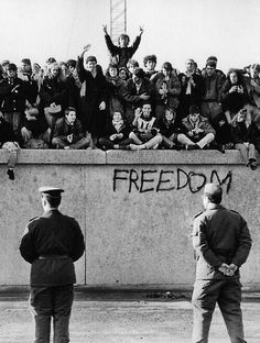 black and white photograph of people standing in front of a wall with the word freedom written on it