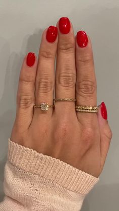 a woman's hand with red nail polish and gold rings on it, holding onto her fingers